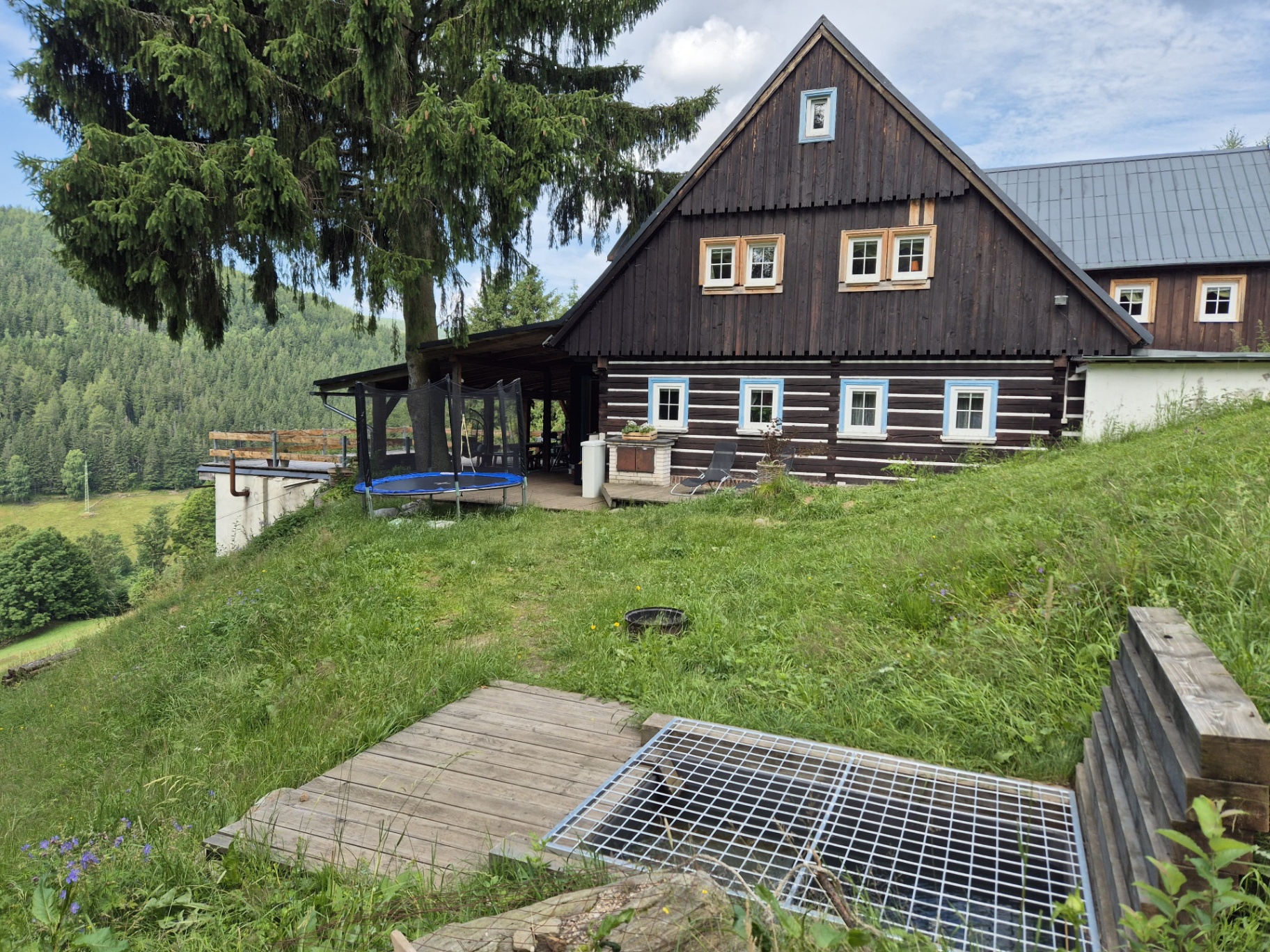 Pohled na chalupu s trampolínou a zastřešeným vchodem